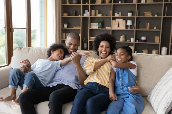 Fröhlich aufgeregte afrikanische Eltern kuscheln, kitzeln Geschwisterkinder auf der Couch — Stockfoto