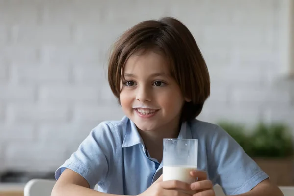 Uroczy chłopiec z wąsami mleka trzyma szklankę napoju mlecznego — Zdjęcie stockowe
