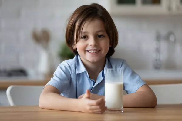 Cute little boy siedzieć przy stole ze szklanką mleka — Zdjęcie stockowe