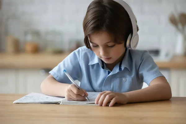 Kleine jongen in koptelefoon met pen schrijven in copybook — Stockfoto