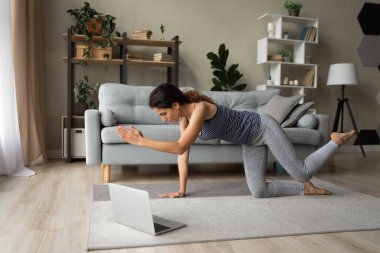 Milenyum Latin kadın dizüstü bilgisayardan önce oturma odasında egzersiz yapıyor.