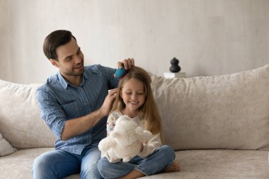 Gülümseyen bekar baba, küçük tatlı kızının saçlarını tarıyor..