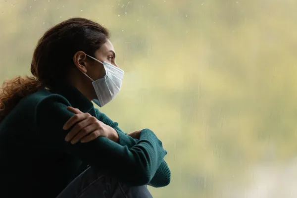 Unhappy latin woman in medical mask spend time by window — Stock Photo, Image