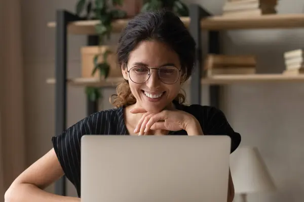 Sonriente millennial latina mujer en gafas uso laptop en escritorio — Foto de Stock