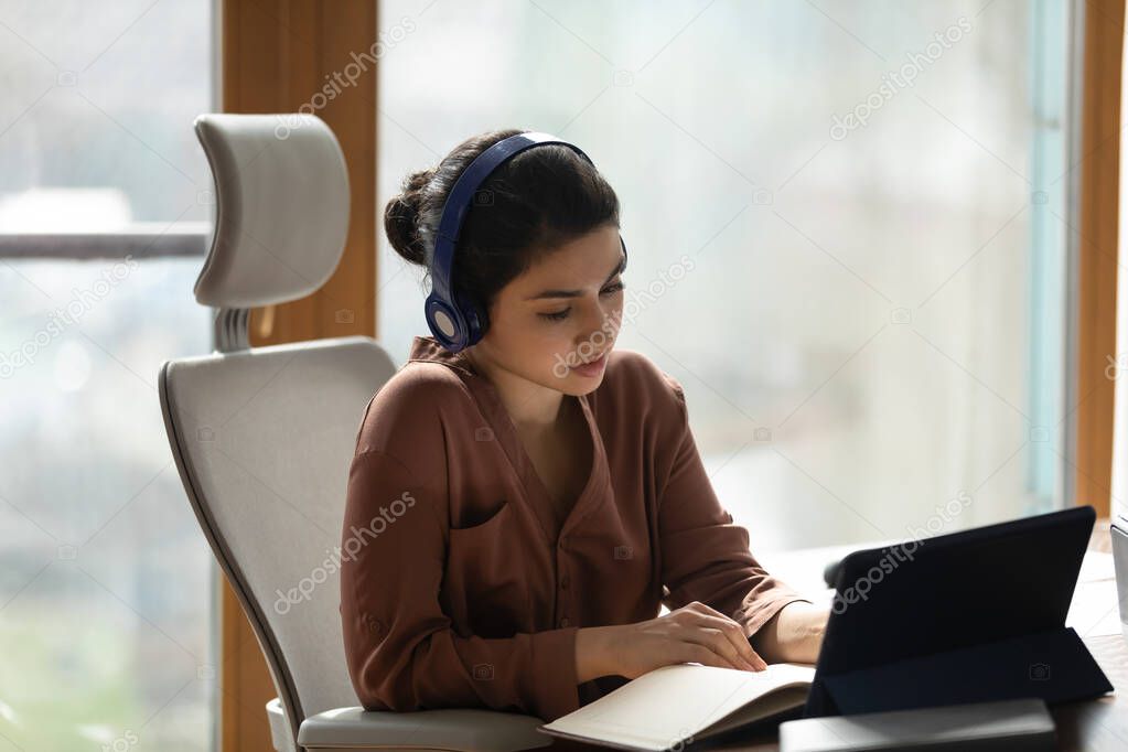 Concentrated young indian woman in headphones listening lecture on touchpad