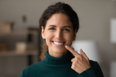 Smiling hispanic lady look at camera point on white teeth clipart