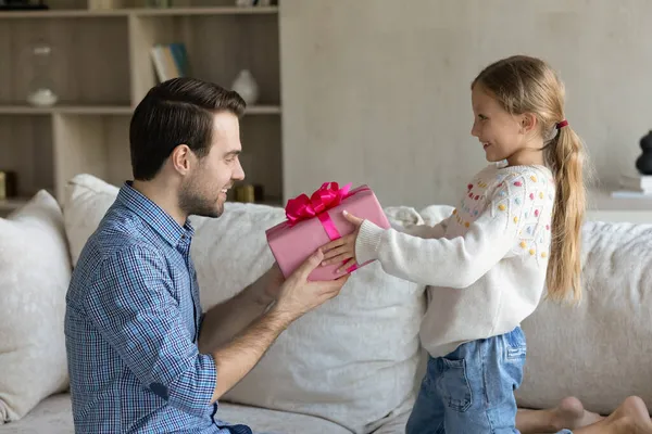 Kleine Tochter überreicht verpackten Geschenkkarton an jungen Vater. — Stockfoto