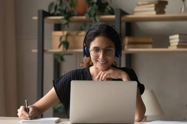 Latijnse vrouwelijke student in hoofdtelefoon luisteren naar de lezing op laptop — Stockfoto