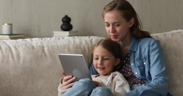 Młoda mama czyta książkę na touchpad razem z małą córką — Wideo stockowe