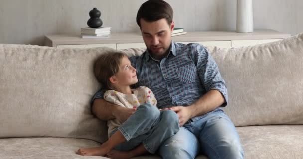 Friendly millennial father talk to little girl on cozy sofa — Stock Video