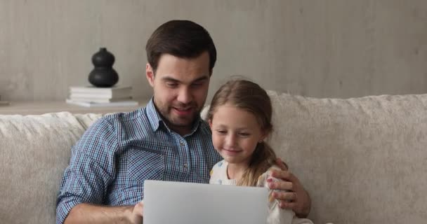 Люблячий батько обіймає дочку, використовуючи ноутбук на затишному дивані — стокове відео