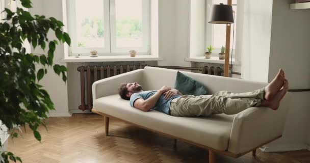 Millennial Kerl schlafen, indem er die Beine auf den Arm von Sofa legt — Stockvideo