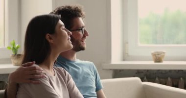 Genç çift kanepede sarılır ve geleceğe bakar.