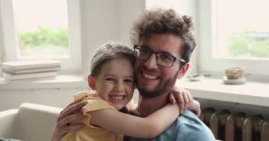 Küçük kızını kucaklayan gülümseyen bir babanın portresi.