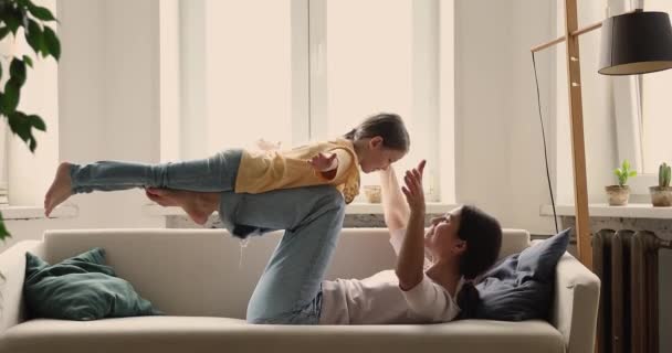 Mamá acostada en la espalda sosteniendo a su hija en el aire en las piernas — Vídeos de Stock