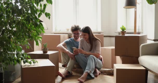 Coppia utilizzando il telefono sul pavimento tra le scatole di nuova casa — Video Stock