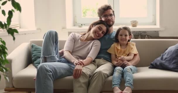 Молодая семейная пара с маленькой дочерью обнимаются на диване — стоковое видео