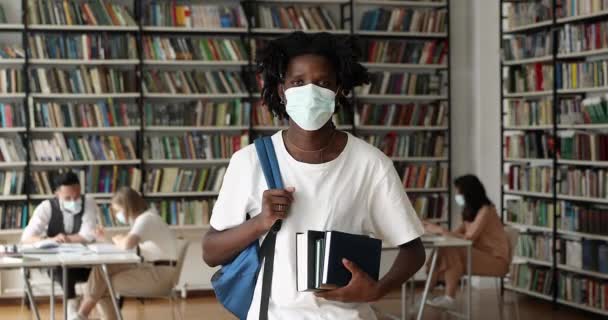 Africano estudiante desgaste mascarilla posando en campus biblioteca — Vídeos de Stock