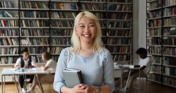 Усміхнений азійський студент тримає підручники в бібліотеці кампуса — стокове відео