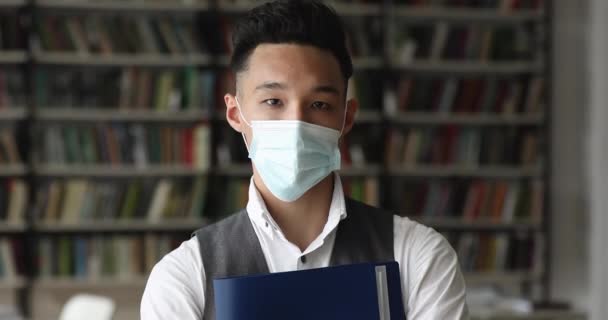 Asiatiska student bär skyddande ansiktsmask poserar i universitetsbiblioteket — Stockvideo