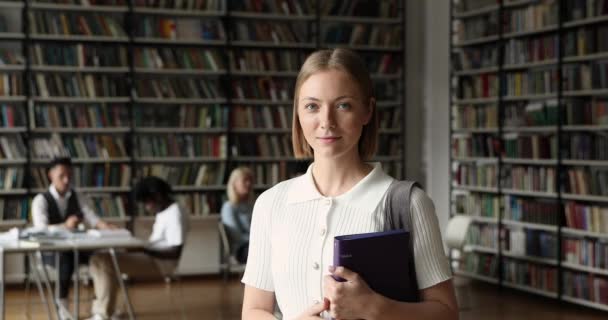 Hermosa sonrisa adolescente chica sostiene carpeta posando en la biblioteca universitaria — Vídeo de stock