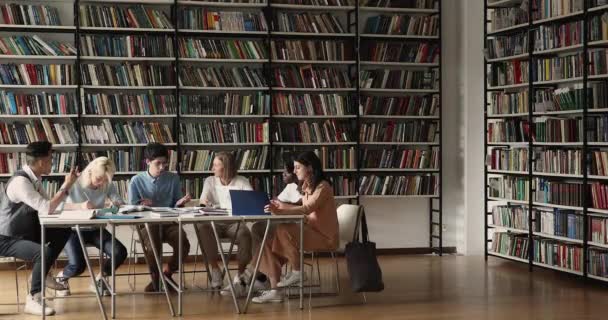 Grupo de compañeros de clase multiétnicos que estudian se sientan en una amplia biblioteca — Vídeos de Stock