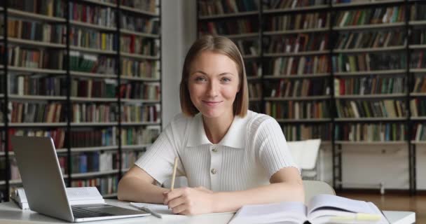 Feliz estudiante niña sentarse en la biblioteca sonrisa mira a la cámara — Vídeo de stock