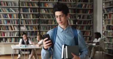 Öğrenci üniversite kütüphanesinde dururken cep telefonu kontrol mesajları tutuyor