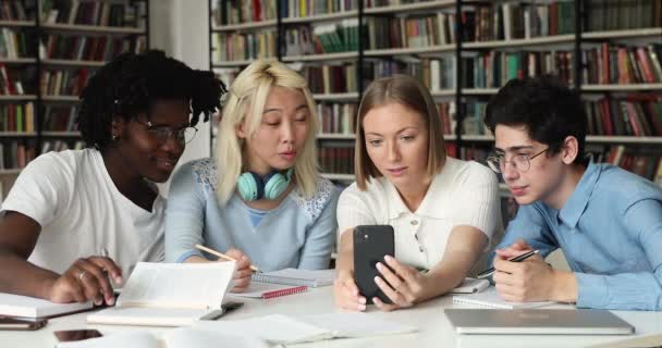 Різні студенти однокласники сидять в бібліотеці весело використовувати мобільний телефон — стокове відео