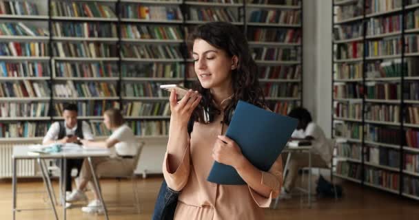 Φοιτητής κορίτσι στέκεται στη βιβλιοθήκη κατέχει ομιλία smartphone σε μεγάφωνο — Αρχείο Βίντεο