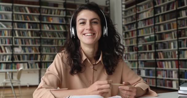 Студент сидить у бібліотеці в навушниках, розмовляє з онлайн репетитором — стокове відео