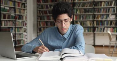 Öğrenci kütüphanede oturur ve kitaptaki başlıkları okur