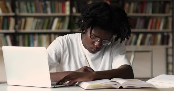 Estudiante africano tomando notas mientras estudia usando laptop — Vídeo de stock