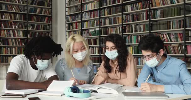 Estudiantes multiétnicos usan mascarillas estudian juntos en la biblioteca — Vídeo de stock