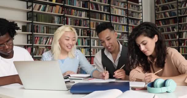 Cuatro compañeros de escuela multirraciales se comunican sentarse en la biblioteca con el ordenador portátil — Vídeos de Stock