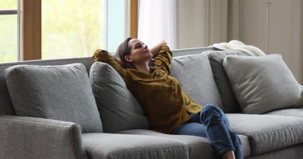 Γαλήνια νεαρή γυναίκα χαλαρώστε στον καναπέ κρατώντας τα χέρια πάνω από το κεφάλι — Αρχείο Βίντεο
