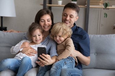 Mutlu ebeveynler ve iki kardeş akıllı telefondan selfie çekiyorlar.