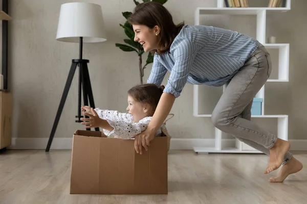 Happy mom laughing, dragging box with screaming little daughter