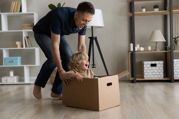 Vrolijke vader verschuiven kartonnen doos met gelukkig zoontje binnen — Stockfoto