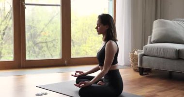 Huzurlu genç kadın Yogi oturma odasında minder üzerinde meditasyon yapıyor.