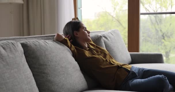 Jovem feliz inclina-se para trás no sofá acolhedor perto da janela — Vídeo de Stock