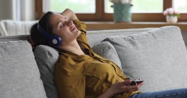 Serene young woman listen to melody on smartphone in headset — Stock Video