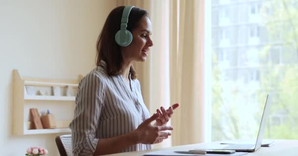Przyjemna młoda kobieta nosić słuchawki porozmawiać z klientem za pomocą laptopa — Wideo stockowe
