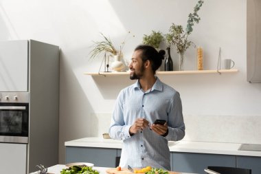 Yemek hazırlamakla meşgul olan mutlu Afro-Amerikan adam cep telefonu kullanıyor..