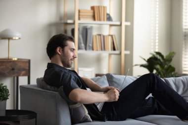 Evdeki kanepede çalışan mutlu, gülümseyen adam.