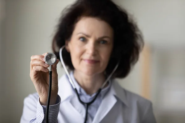Gammal kvinnlig GP läkare hand hålla stetoskop närbild objekt — Stockfoto