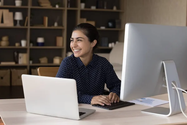 Happy millennial Indian employee satisfied with job, working at laptop