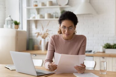 Gözlüklü gülümseyen kadın belgelerle çalışıyor, dizüstü bilgisayar kullanıyor.