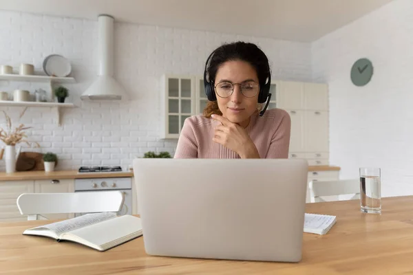 Зосереджена жінка в гарнітурі дивиться на екран ноутбука, вивчаючи онлайн — стокове фото