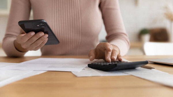 Close up cropped of woman using smartphone, calculating bills